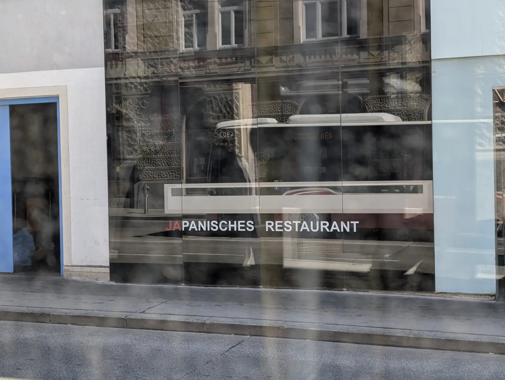 Foto von einer Glaswand, auf der "JAPANISCHES RESTAURANT" steht. Das "JA" ist rot, die restliche Schrift ist weiß, daher sieht es aus wie "JA PANISCHES RESTAURANT".