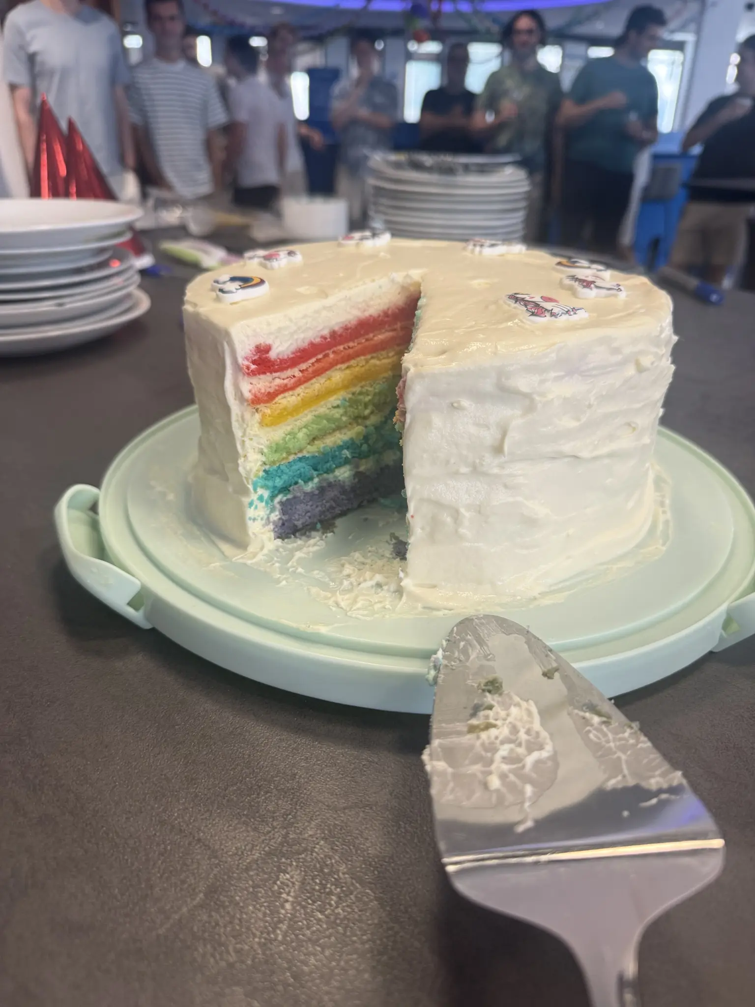 Rainbow cake with one slice missing showing the rainbow layers inside a white frosting