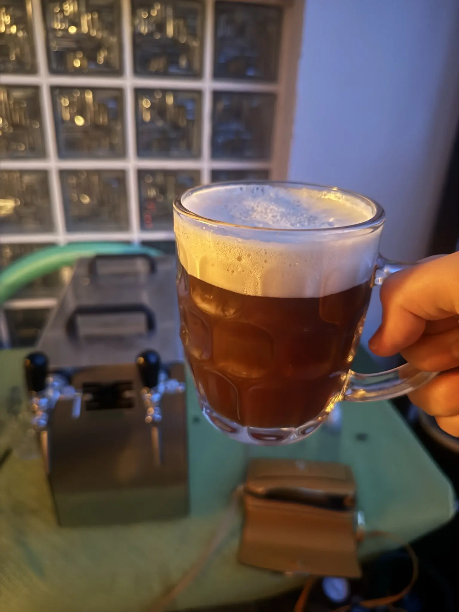 Ein Bierglas mit einem dunklen Bier mit dicken Schaum vor einem Durchlaufkühler