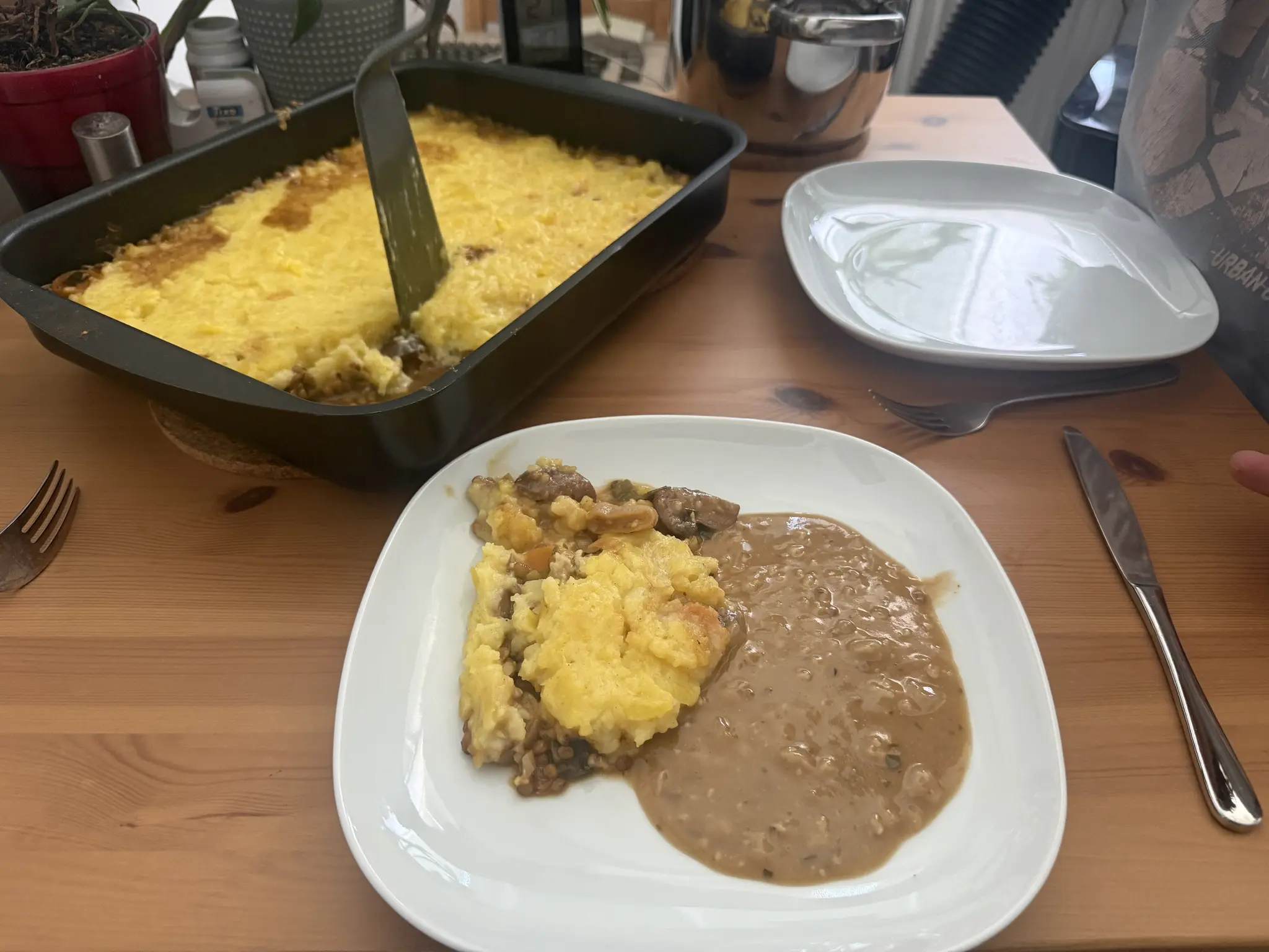 A plate with lentil sheperd‘s pie and gravy, behind that a big pan full of pie