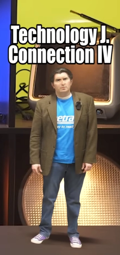 Screenshot of a youtube video. A small, short-haired, light-skinned man labelled "Technology J. Connection IV" is standing on a desk. This is Alec from Youtube channel "Technology Connections", but his face was edited heavily.
